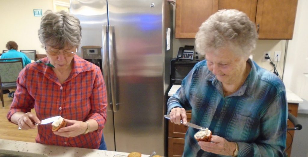 Two enhanced assisted living residents frost cupcakes together.